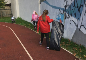 Dziewczynki szukają śmieci na terenie boiska.