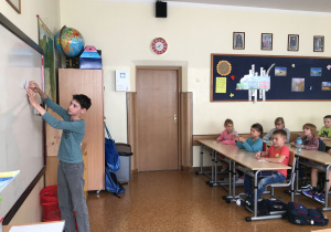 Adam pokazuje na tablicy kolejność składania papierowej łódki.