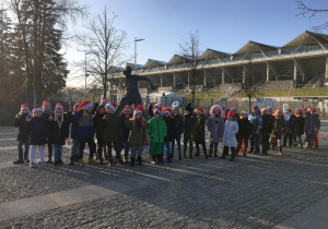Drugoklasiści stoją pod pomnikiem Kazimierza Deyny.