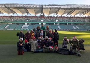 Klasa 2b stoi przy murawie boiska i pozuje do zdjęcia grupowego na tle napisu Legia.