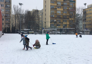 Dzieci wzajemnie wożą się na sankach.