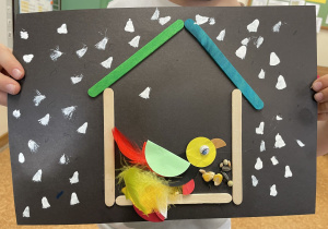 Uczennica prezentuje swoją pracę - Ptaszek z kółek origami i piórek w karmniku.