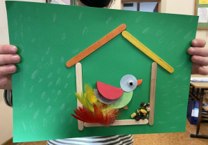 Uczeń prezentuje swoją pracę - Ptaszek z kółek origami i piórek w karmniku.