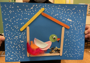 Uczeń prezentuje swoją pracę - Ptaszek z kółek origami i piórek w karmniku.