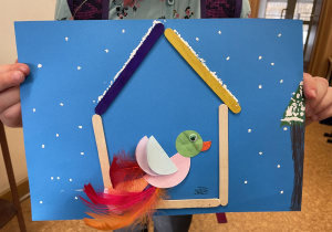 Uczennica prezentuje swoją pracę - Ptaszek z kółek origami i piórek w karmniku.