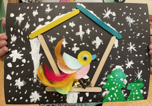 Uczennica prezentuje swoją pracę - Ptaszek z kółek origami i piórek w karmniku.