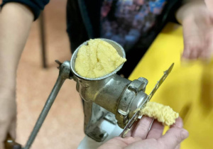 Uczeń kręci ciastko z niezwykłą dbałością o to, aby się udało. Na pierwszym planie widać maszynkę do kręcenia ciastek.