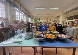 Zdjęcie grupowe dzieci z obu klas. Na pierwszym planie stół z przygotowanymi produktami do wyciskania soków.