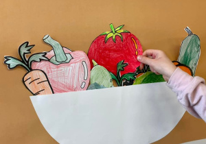 Uczeń wkłada wyciętego pomidora do misi przyczepionej do tablicy.