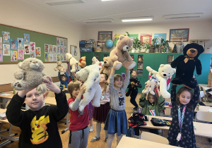 Dzieci prezentują swoje misie unosząc je do góry nad głowami.