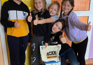 Uczniowie stoją z karmą dla psów i przypominają o trwającej zbiórce darów dla podopiecznych ze schroniska w Celestynowie.