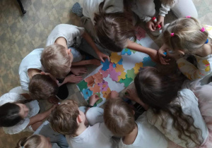 Grupka uczniów układa i przykleja do papieru puzzle integracyjne.