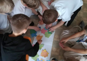 Grupka uczniów układa i przykleja do papieru puzzle integracyjne.