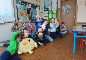 Uczniowie z klasy 1b siedzą w klasie i prezentują swoje Misie.
