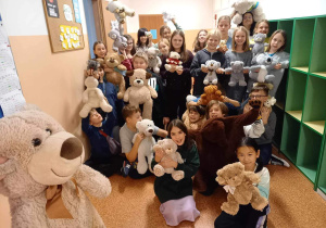 Uczniowie z klasy 5b stoją na korytarzu i prezentują swoje Misie.