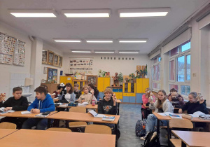 Uczniowie z klasy 7a siedzą w ławkach i prezentują swoje Misie.