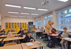 Uczniowie z klasy 8b siedzą w ławkach i prezentują swoje Misie.
