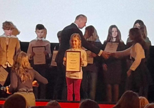 Uczennica z naszej szkoły prezentuje na scenie dyplom.