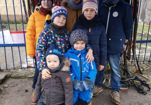 Uczniowie z młodszym rodzeństwem stoją przy furtce schroniska.