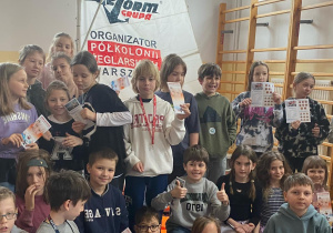 Uczniowie z klas trzecich pozują do zdjęcia, w rękach trzymają ulotki informujące o programie edukacyjnym.