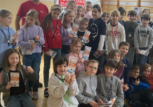 Uczniowie z klas trzecich pozują do zdjęcia, w rękach trzymają ulotki informujące o programie edukacyjnym.