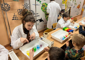 Starsi uczniowie, pod czujnym okiem nauczycieli, pokazują młoszym kolegom chemiczne eksperymenty.