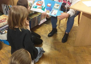 Pani Bibliotekarka pokazuje dzieciom zdjęcia z książki o sportach zimowych.