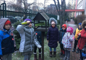 Uczennica czyści karmnik przygotowując go do wsypania pestek słonecznika i dyni dla ptaków.