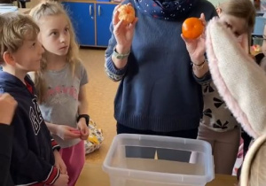 Pani Sylwia pokazuje uczniom co trzyma w rękach i tłumaczy zasady eksperymentu.