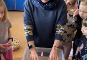 Pani Sylwia wkłada dwie mandarynki do naczynia wypełnionego wodą. Jedna mandarynka jest obrana, drugia nie.