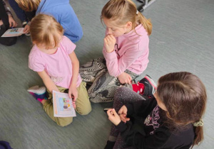 Dziewczynki siedząc na podłodze przeglądają książeczkę na temat przestrzeni osobistej.