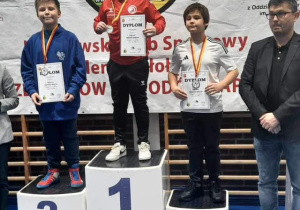 Karol, po dekoracji medalami, stoi na podium i w rękach trzyma dyplom.