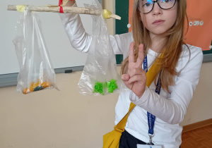 Hanna stoi przed tablicą i pokazuje efekt zważenia dinozaura.