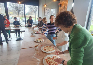 Wychowawczyni wraz z uczniami przyrządza pizzę.