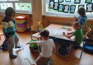 Uczniwoie siedzą przy ławkach i nawlekają na sznurki kolorowe dziesiątki z makaronu.