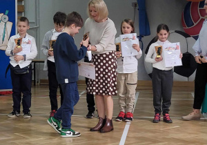 Dzieci stoją w sali gimnastycznej. nauczycielka wręcza nagrodę i dyplom Frankowi.