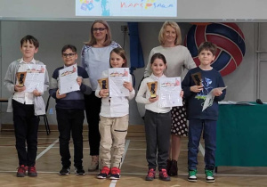 Dzieci stoją w sali gimnastycznej i prezentują swoje nagrody.