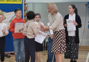 Uczniowie stoją w sali gimanstycznej. Nauczycielka wręcza nagrodę Matt'owi.