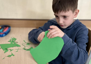 Maksym wycina elementy ciała żaby z kartonu w kolorze zielonym - brzuszek.