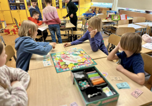 Uczniowie siedzą przy stoliku i grają w Monopoly Squishmallows.
