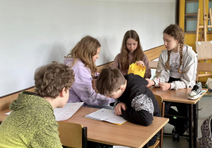 Grupa uczniów siedzi w ławkach i przygotowuje się do pokazu.