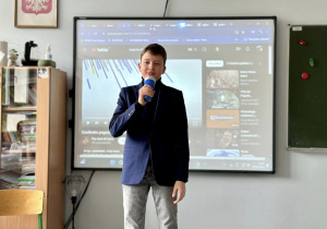 Samuel, w roli prezentera telewizji śniadaniowej, zapowiada pokaz swojej grupy.