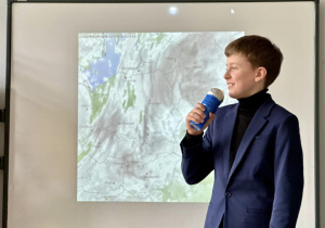 Samuel, w roli prezentera telewizji śniadaniowej, zapowiada pogodę.
