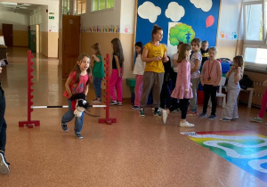 Uczennica rozpoczęła bieg przez przeszkody. Pozstali uczniowie czekają na swoją kolej.