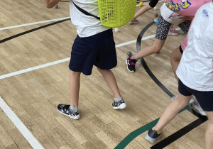 Uczniwoie podcza gry ruchowej zbierają kolorowe piłeczki do plastikowych koszyczków.