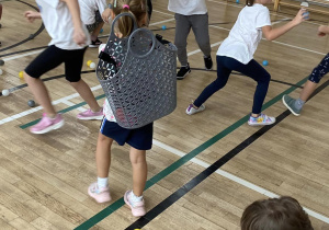 Uczniwoie podcza gry ruchowej zbierają kolorowe piłeczki do plastikowych koszyczków.