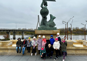 Drugoklasiści stoją pod pomnikiem Syreny i pozują do grupowego zdjęcia.