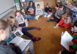 Uczennica czyta na głos fragment swojej ulubionej bajki. Pozostałe dzieci siedzą w kole i słuchają.