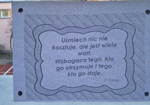 Na szkolnym korytarzu, w oknie wisi przysłowie "Uśmiech nic nie kosztuje, ale jest wiele wart. Wzbogaca tego, kto go otrzymuje i tego, kto go daje".