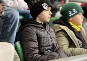 Uczniowie siedzą na trybunie stadionu i słuchają historii klubu.